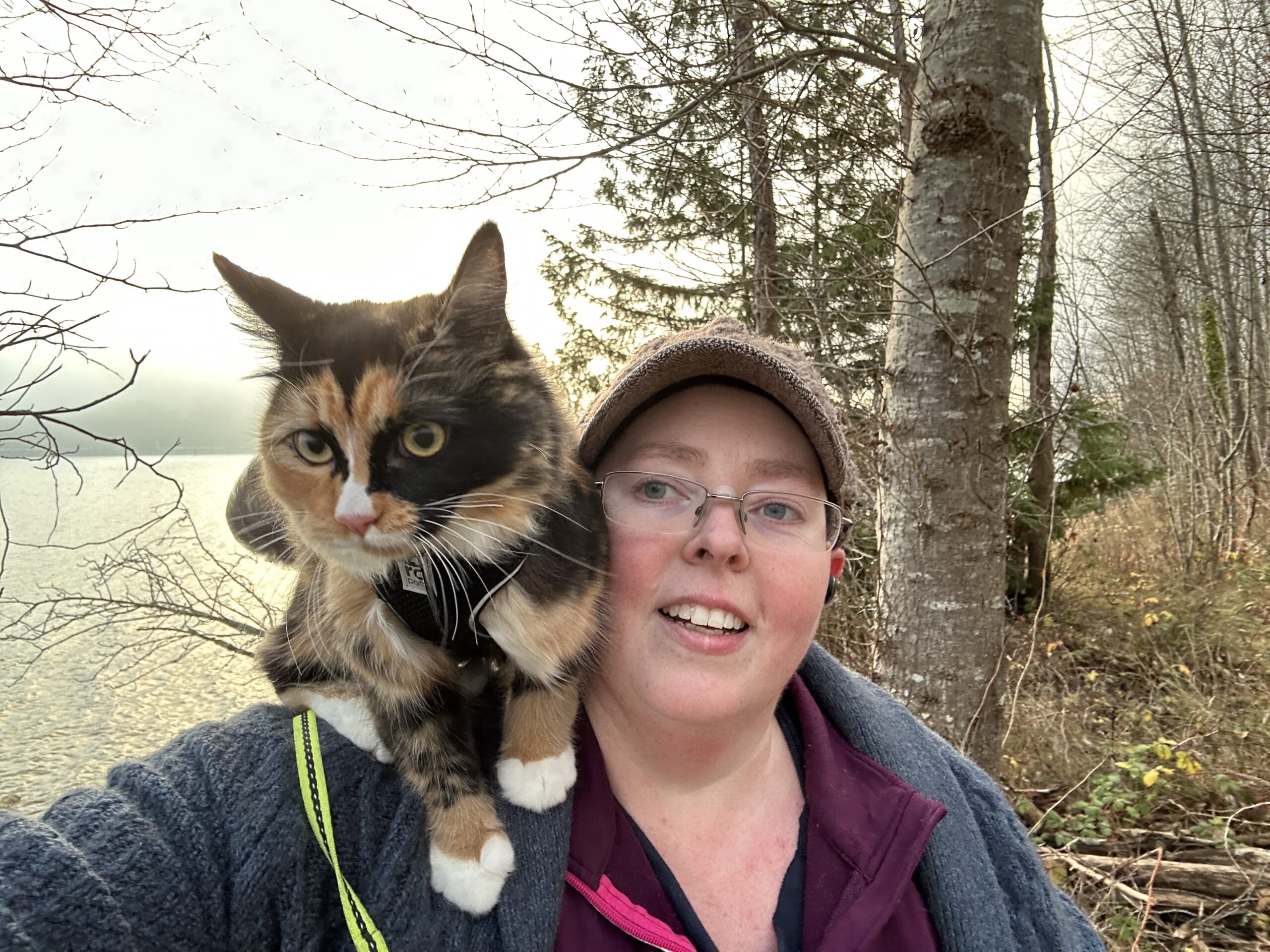Heather's leashed cat, Talula Belle, is on their shoulder. They are outdoors in a park.