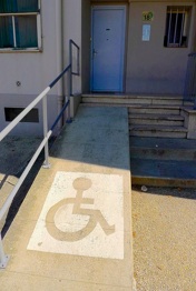 a photograph of a ramp going up the left side of a flight of stairs. a railing is to the left of the ramp, and a blue door is directly at the top of the ramp.