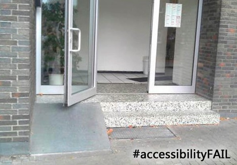 A photograph of a short ramp going up two steps, being blocked by an open door