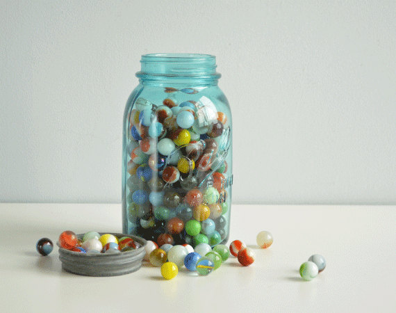 a photograph of a glass jar filled with colourful marbles, with some scattered outside the jar